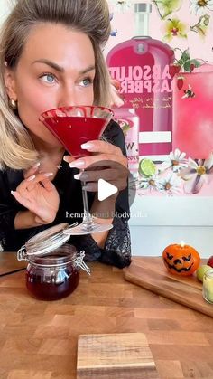 a woman sitting at a table with a drink in front of her face and halloween decorations on the wall behind her