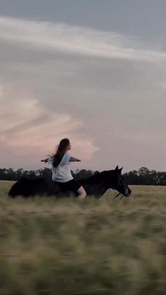 a woman riding on the back of a black horse through a grass covered field at sunset