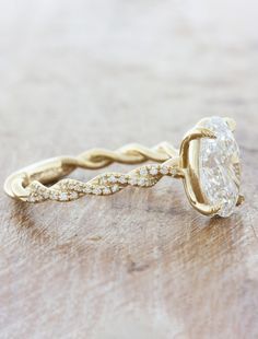 a yellow gold ring with an oval cut diamond in the center on a wooden surface