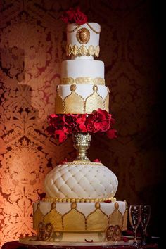 a three tiered wedding cake with red flowers on top and gold trimmings