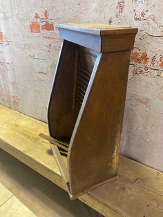 a wooden bench with a magazine holder on it's back and an old brick wall in the background