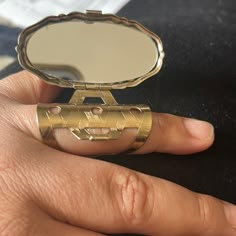 a person's hand holding a gold ring with a mirror on top of it