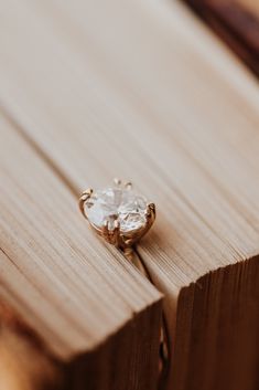 an engagement ring sitting on top of a piece of wood with a diamond in the middle