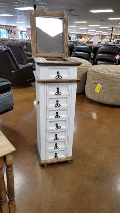 a white dresser with drawers and a mirror on it in a room filled with couches