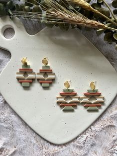 three pairs of earrings sitting on top of a white platter next to dried flowers