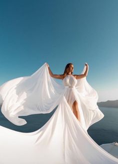 a woman in a white dress is standing on the edge of a cliff by the ocean