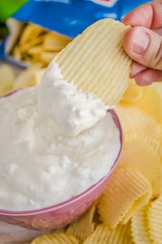 a hand holding a cracker over a bowl of chips with dip in the middle