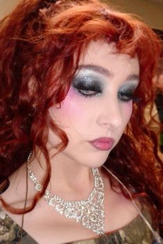 a woman with red hair and blue eyeshadow is wearing a necklace on her neck