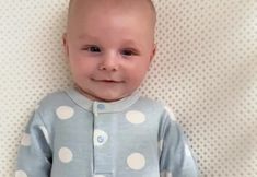 a smiling baby wearing a blue and white polka dot pajamas on top of a bed