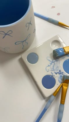 three paintbrushes sitting on top of a white table next to a blue cup