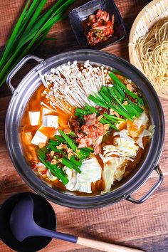 an overhead view of a bowl of soup with chopsticks and green onions on the side