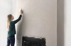 a woman is painting the wall in her living room with white paint and a fireplace