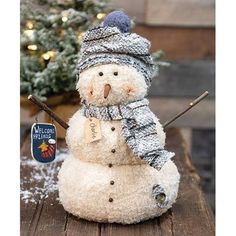 a snowman with a hat and scarf on sitting in front of a christmas tree