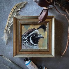 a painting of a bird is hanging in a frame next to some paint and brushes