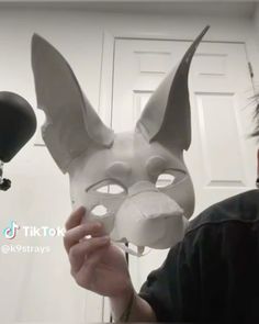 a man is holding up a mask that looks like a cat's head and ears