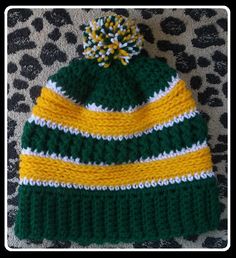 a green, yellow and white knitted hat laying on top of a leopard print blanket