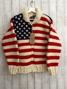 an american flag sweater hanging on a white wooden wall with a tag attached to it