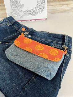 an orange and yellow purse sitting on top of some blue jeans next to a book