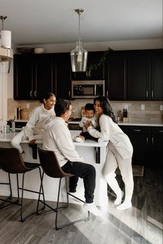 three people sitting at a kitchen counter with one person holding a baby and the other standing up