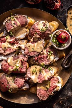 a plate full of meat and potatoes covered in gravy next to some dipping sauce