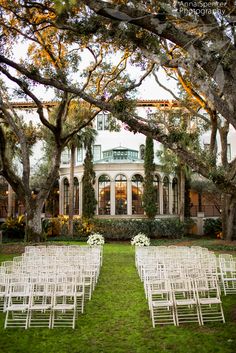 white chairs are set up in front of a large building with trees and flowers on the lawn