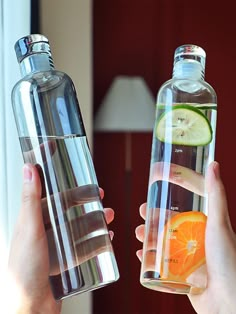 two people holding up water bottles with fruit in them