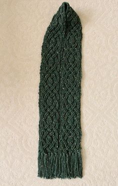 a green knitted scarf laying on top of a white floor next to a wall