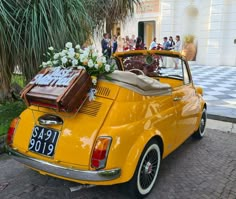 an old yellow car with luggage on the back