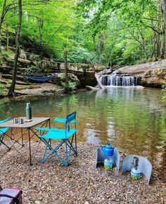 there is a picnic table and chairs by the water with a waterfall in the background