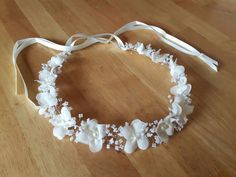 a white headband with flowers and pearls is on a wooden floor next to a ribbon