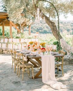 an outdoor table set up for a wedding reception with chandelier hanging from the tree