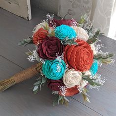 a bridal bouquet with red, white and blue flowers on a wooden table next to a window