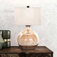 a glass lamp sitting on top of a wooden table next to two vases and a book