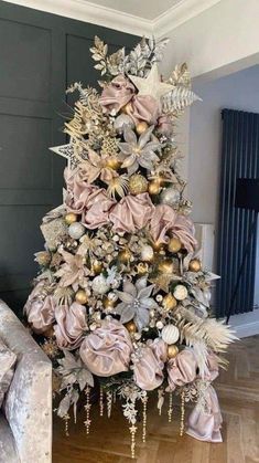 a christmas tree decorated with gold ornaments and pink bows is in the middle of a living room