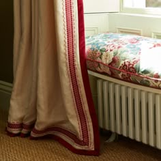 a bed sitting next to a window in a room with a red and white blanket on top of it