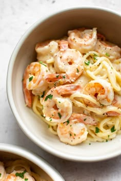 two bowls filled with pasta and shrimp on top of a white countertop next to each other