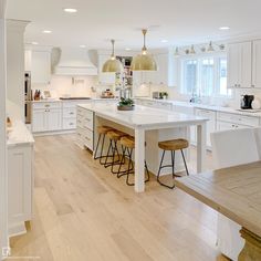 a large kitchen with white cabinets and counter tops, an island in the middle is surrounded by bar stools