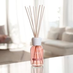 a pink bottle filled with reeds sitting on top of a table next to a white couch