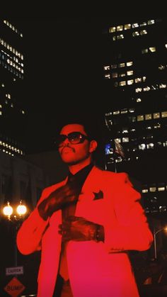 a man in a red suit and sunglasses is posing for the camera with his hand on his tie