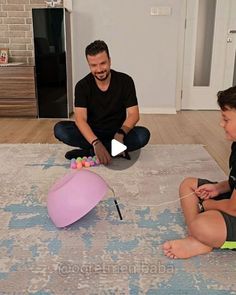 two men are sitting on the floor playing with an interactive balloon golf ball game while another man watches