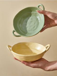 two hands are holding bowls in front of each other, one is green and the other is yellow