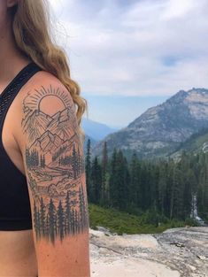 a woman with a tattoo on her arm looking at the mountains and trees in the distance