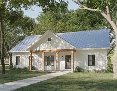 a small white house with a porch and covered veranda in the front yard, surrounded by trees