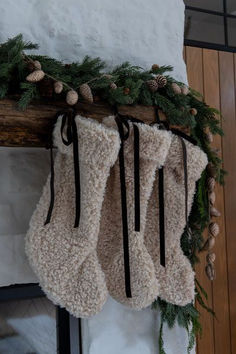 three stockings hanging from a fireplace with pine cones