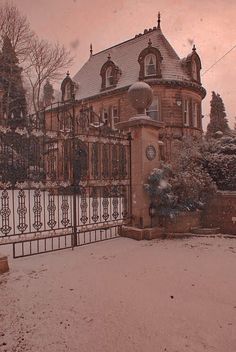 a large building with a gate and snow on the ground in front of it, surrounded by trees