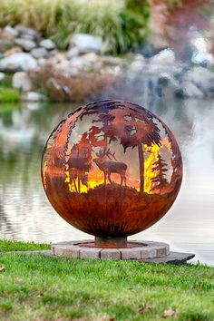 a metal sculpture sitting on top of a lush green field next to a lake and forest