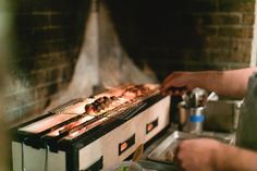 a man cooking food on top of a grill next to a brick wall in a kitchen