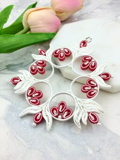 a red and white brooch sitting on top of a table next to tulips