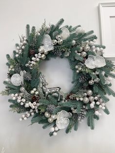 a christmas wreath hanging on the wall next to a white frame with silver ornaments and pine cones