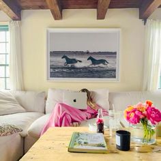 a woman sitting on a couch in front of a table with vases and flowers